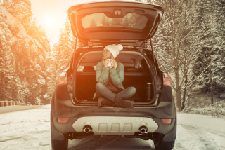 Person sitting in the open trunk of a vehicle on a snowy road, representing auto insurance coverage